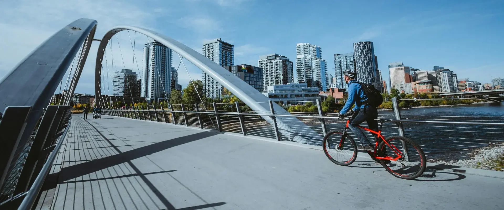 Cyclist and pedestrians on the Skipping Stone Bridge over the Bow River, Calgary, looking toward East Village